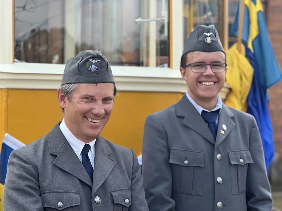 Två spårvagnsförare i grå uniform framför veteranvagn
