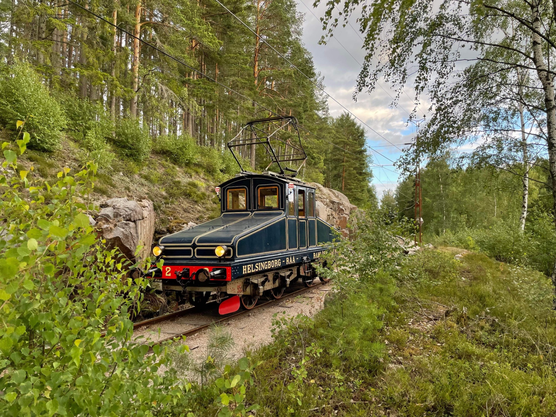 Mörkblått veteranellok från Helsingborg–Råå–Ramlösa på spår i skogen