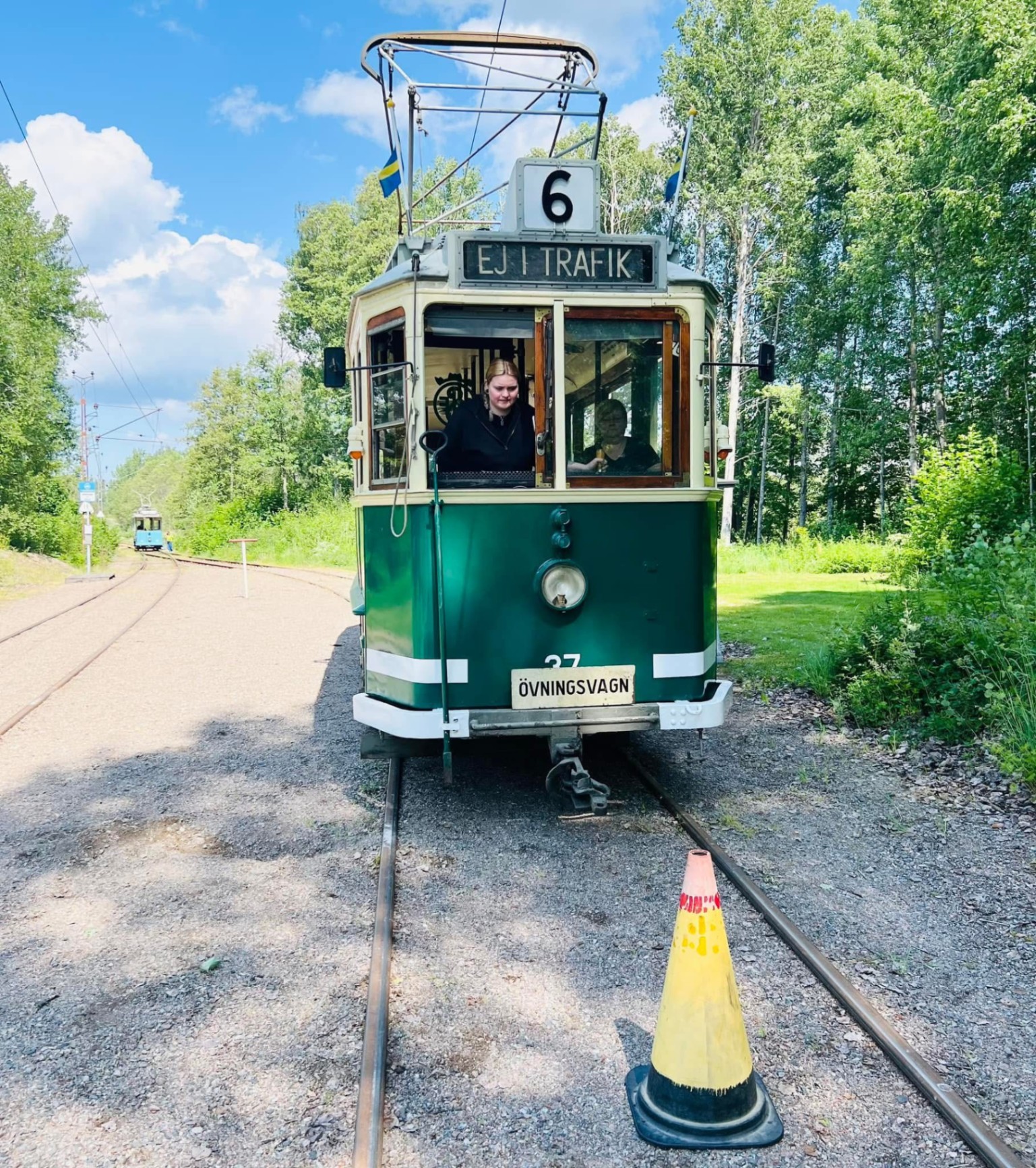 Grön övningsvagn nummer 37 vid spårväg i sommarmiljö