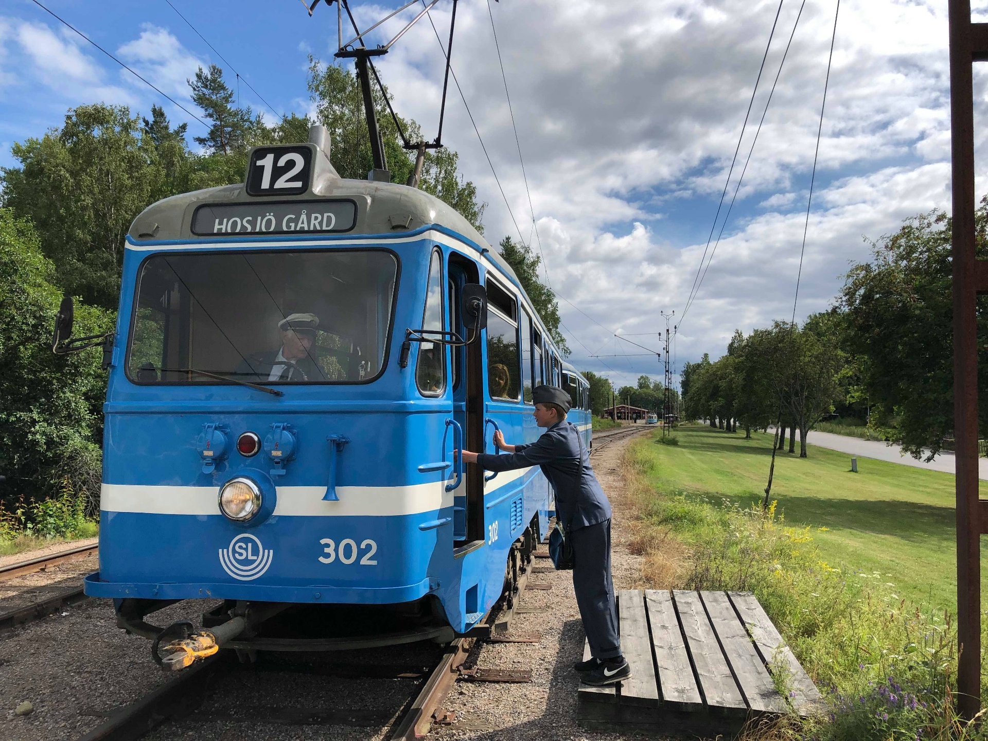 Blå SL-spårvagn 302 mot Hösjö gård med konduktör i uniform